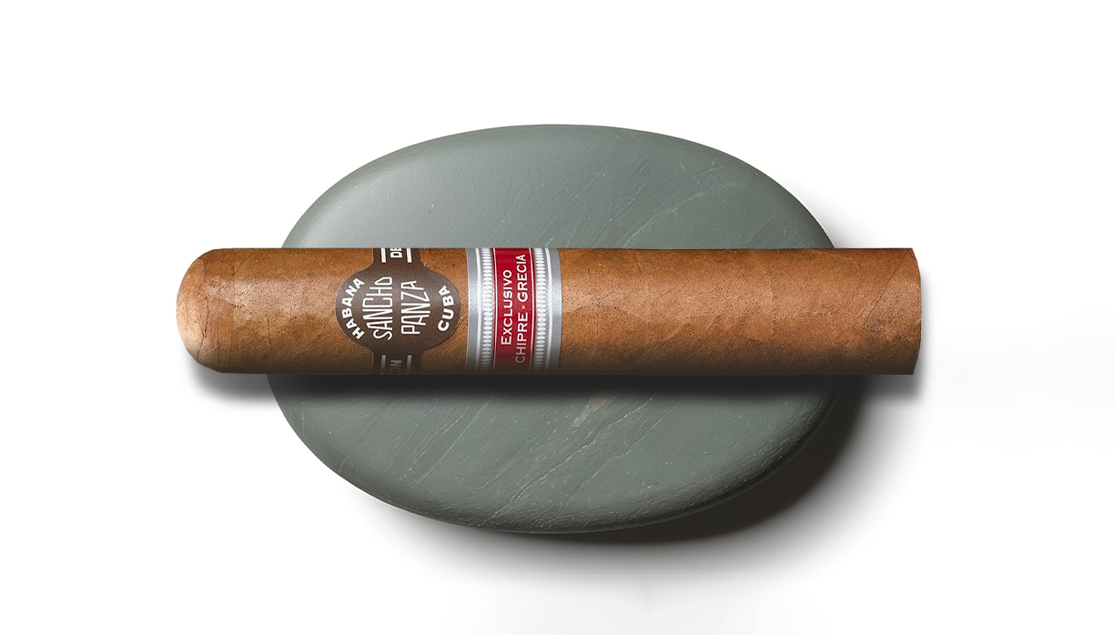 サンチョ・パンサ、茶帯に「SANCHO PANZA」「HABANA」と赤の「EXCLUSIVO CHIPRE-GRECIA」副帯、薄茶ラッパーを灰色の石に載せた白背景。